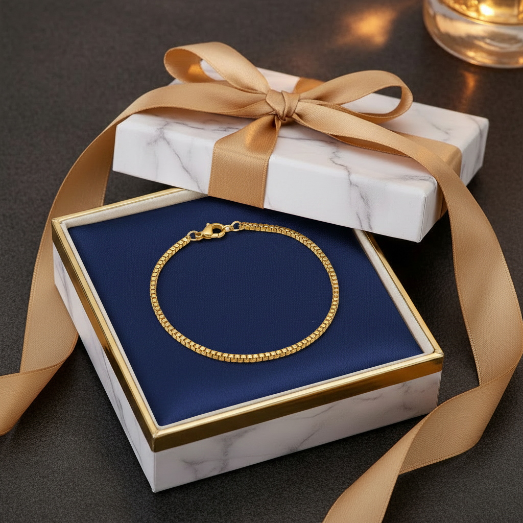 Gold box chain bracelet in marble gift box with navy satin interior and gold ribbon on black background