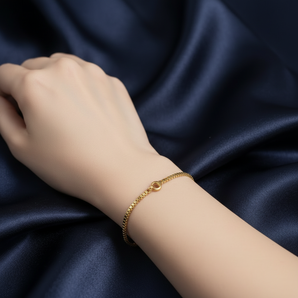 Gold box chain bracelet worn on wrist with navy satin background